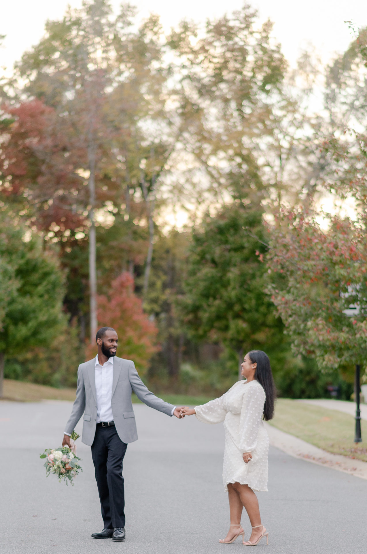 Groom holding his brides bouquet in one hand & holding his brides hand in the other guiding her across the street.